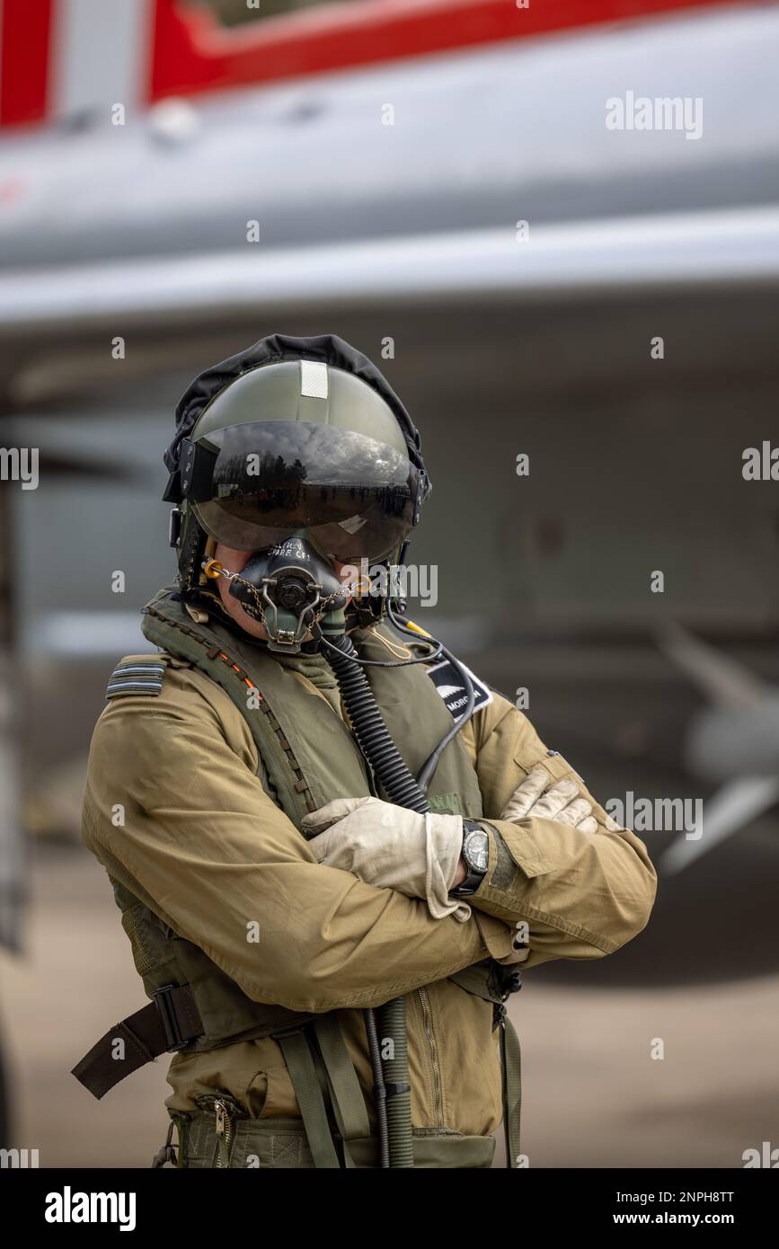 Military Fighter Pilot with helmet, visor and oxygen mask in flying suit with fighter jet in the background. Top gun pose for combat pilot Stock Photo
