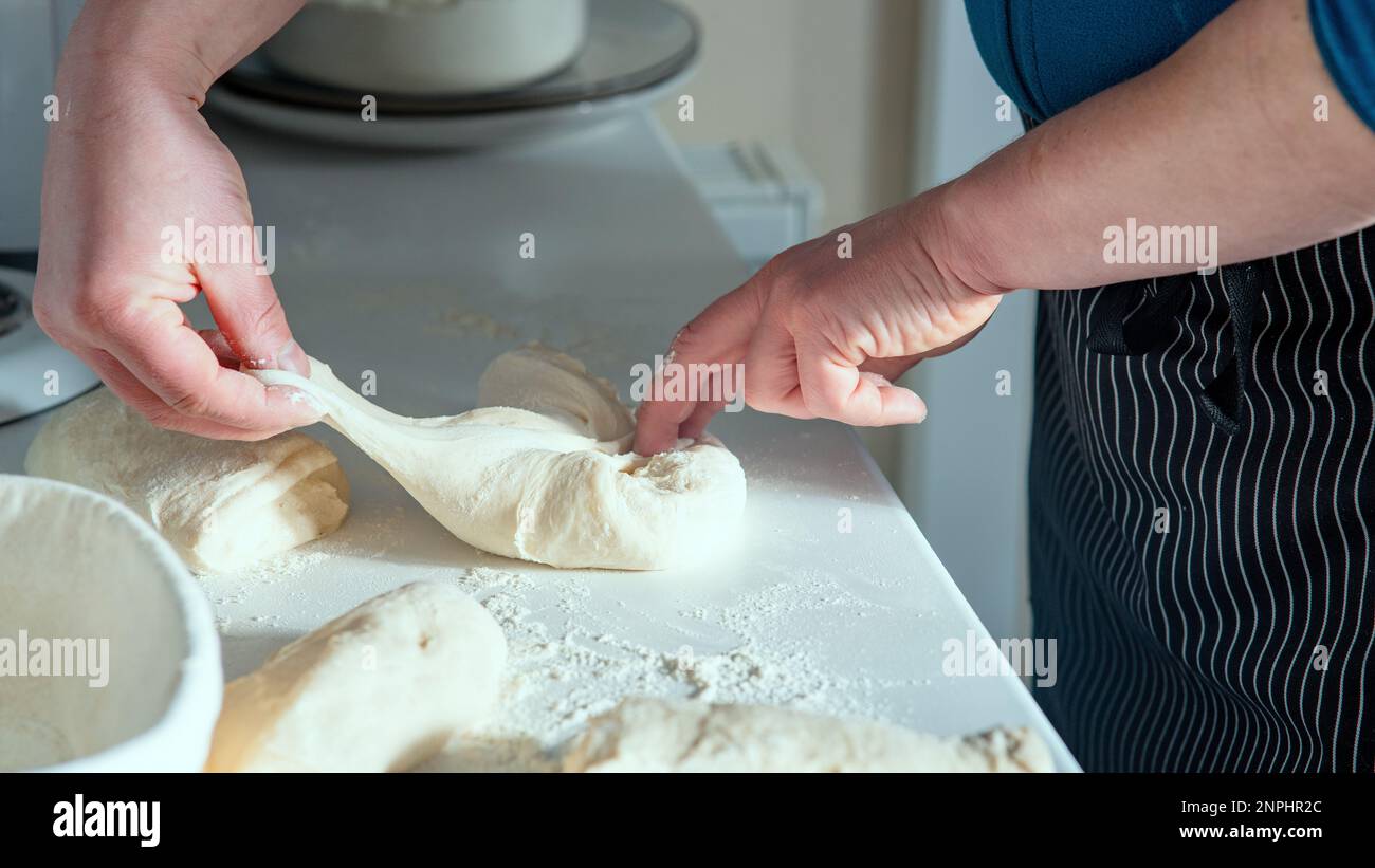 Chef Stretching and folding bread dough on top of white table with