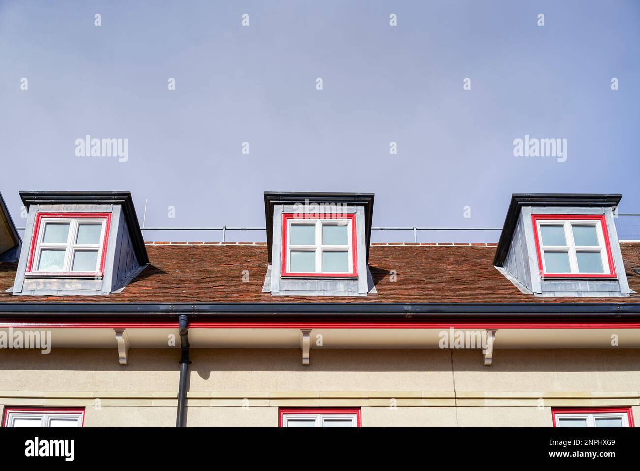 Dormer windows set into a clay tiled roof with blue sky behind Stock Photo
