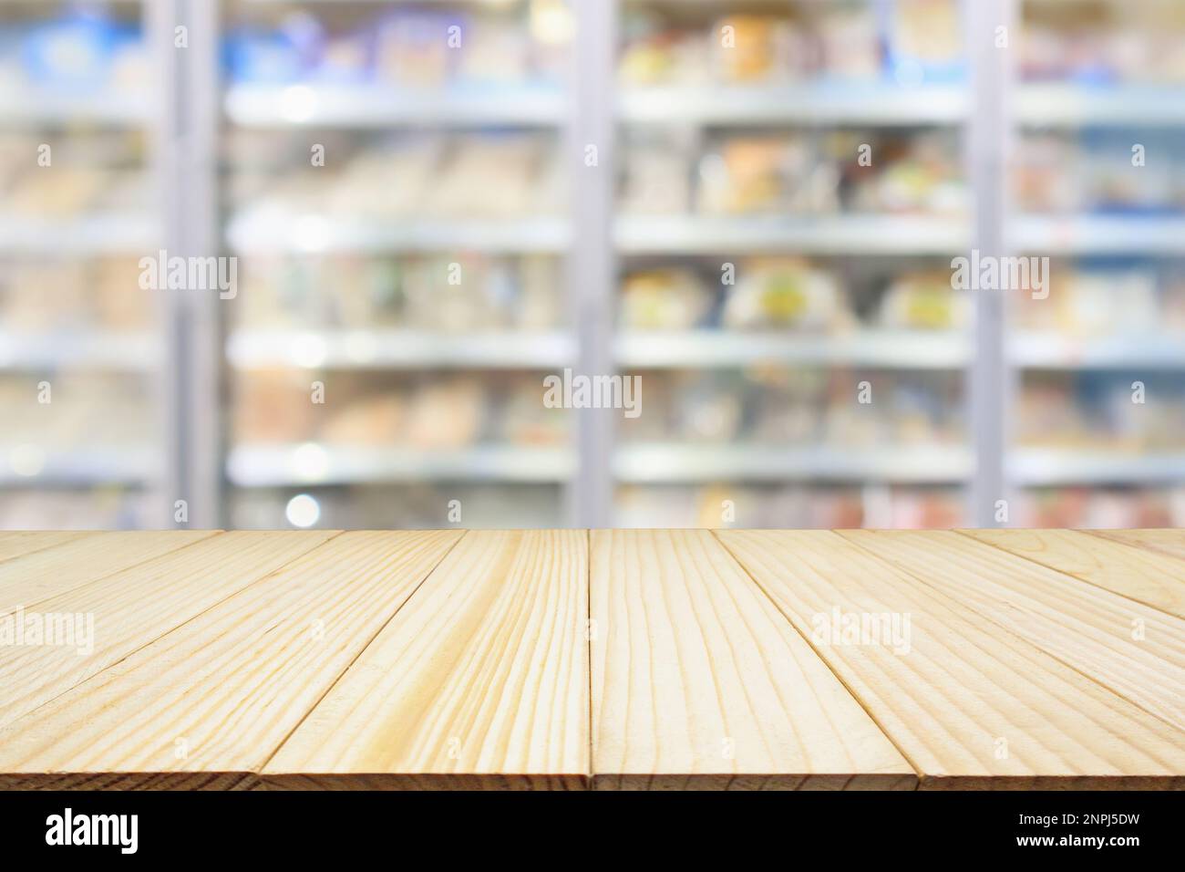 wood table with supermarket commercial refrigerators freezer showing frozen foods abstract blur background Stock Photo