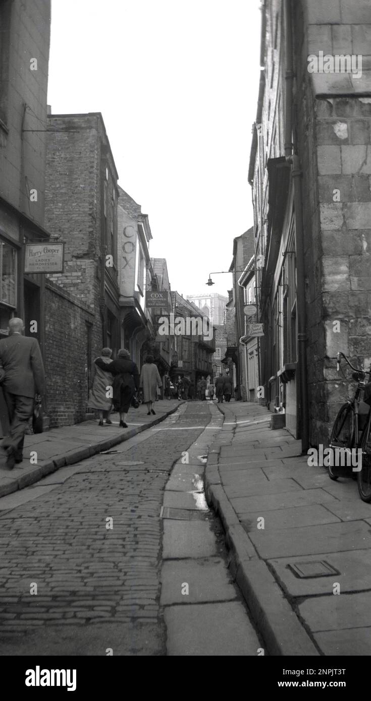 1950s, historical, a view from ground level, upwards of The shambles, a narrow old medieval cobbled street in York, England, UK. Seen on the left of the picture the leather shop, Cox of Northampton, established by William Cox, a shoe repairer and boot-maker by trade in 1921, who had moved to the cathedral city. The shop traded for 93 years, before closing in 2014. Stock Photo