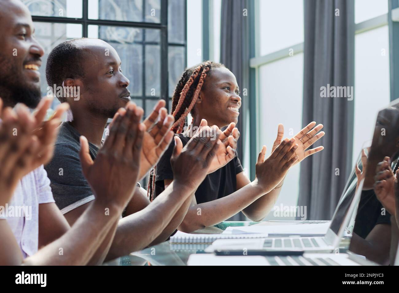 Multi ethnic business group greets somebody with clapping and smiling Stock Photo