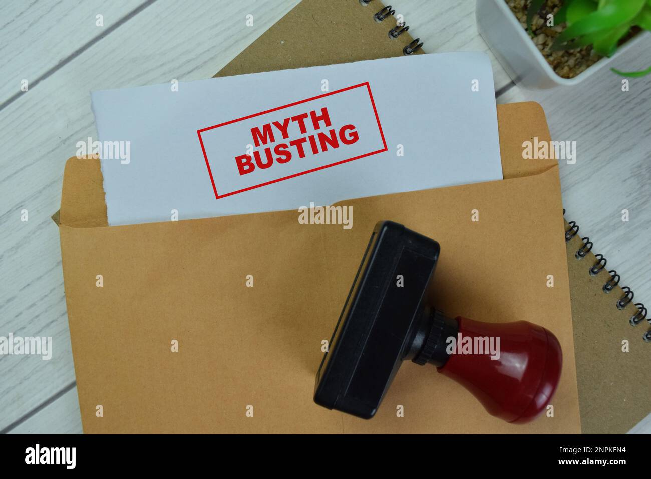 Concept of Red Handle Rubber Stamper and Myth Busting text above Brown envelope isolated on on Wooden Table. Stock Photo