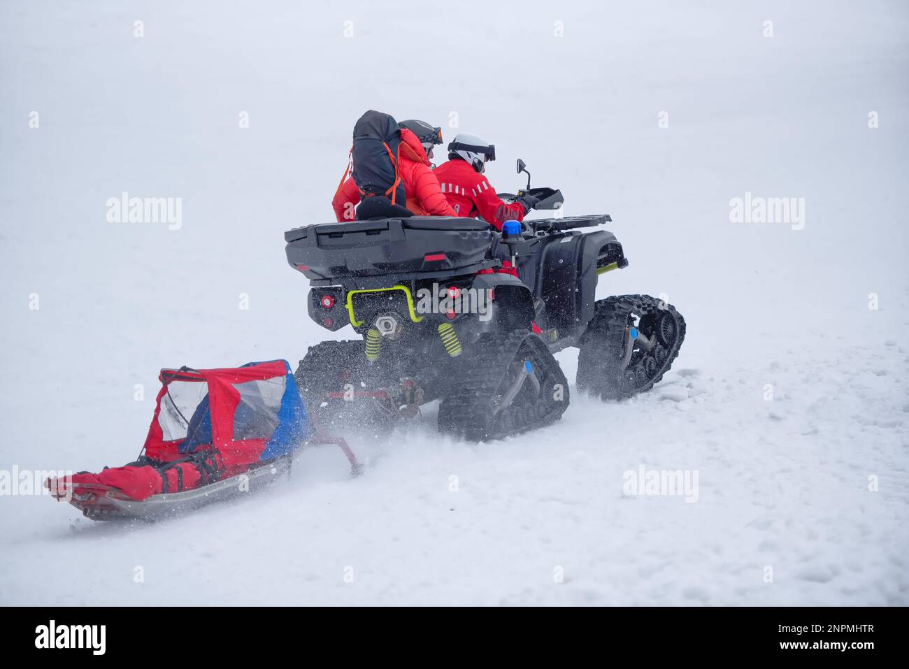 The mountain rescue team is heading out to save a person in the mountains during winter, using a tracked vehicle and a sled Stock Photo