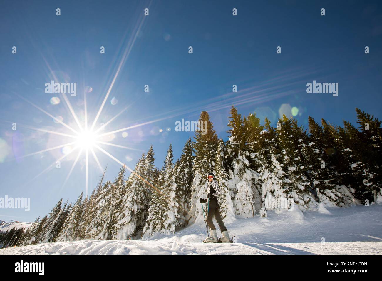 A single young female enjoys a sunny winter day of skiing, dressed in full snow gear with ski boots and sunglasses Stock Photo