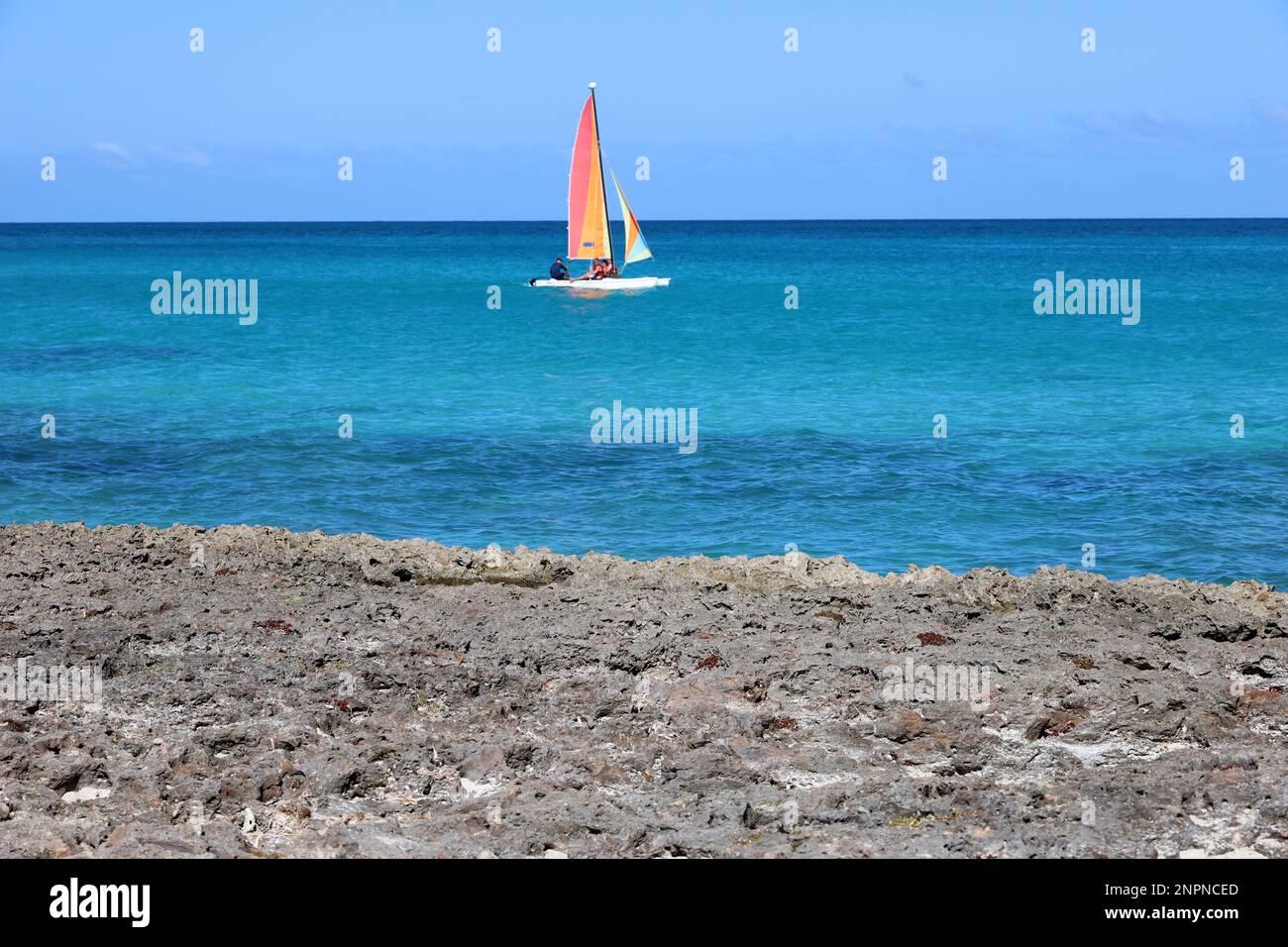 Defocused view to blue ocean with sailboat from stone coast. Background for holidays on a sunny nature Stock Photo