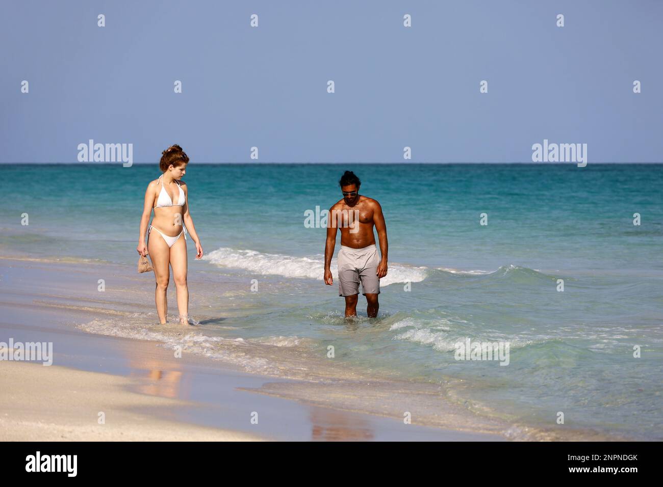 Interracial couple on a beach, white woman in bikini and black man walking in ocean water Stock Photo