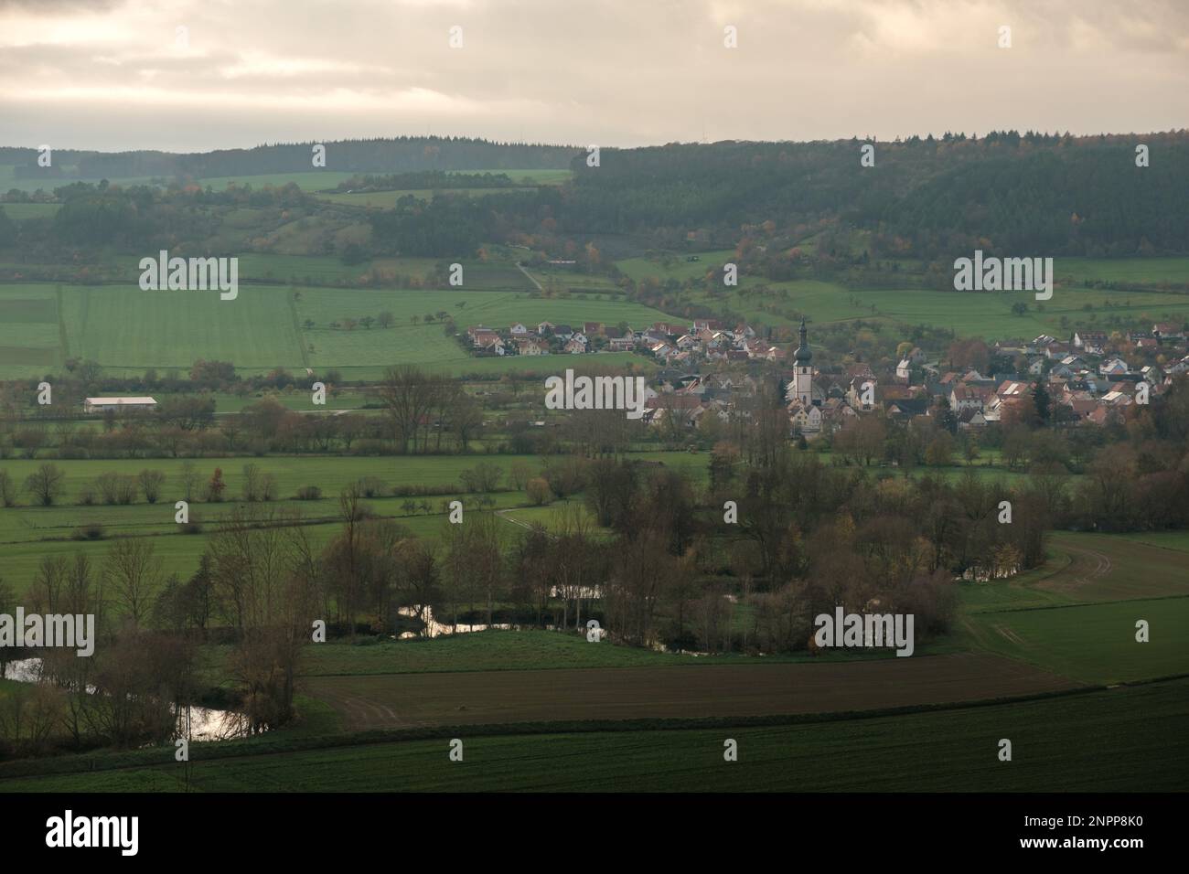View over the meadows and fields to the river Tauber with the small village of Hochhausen in the background at sunset. Stock Photo