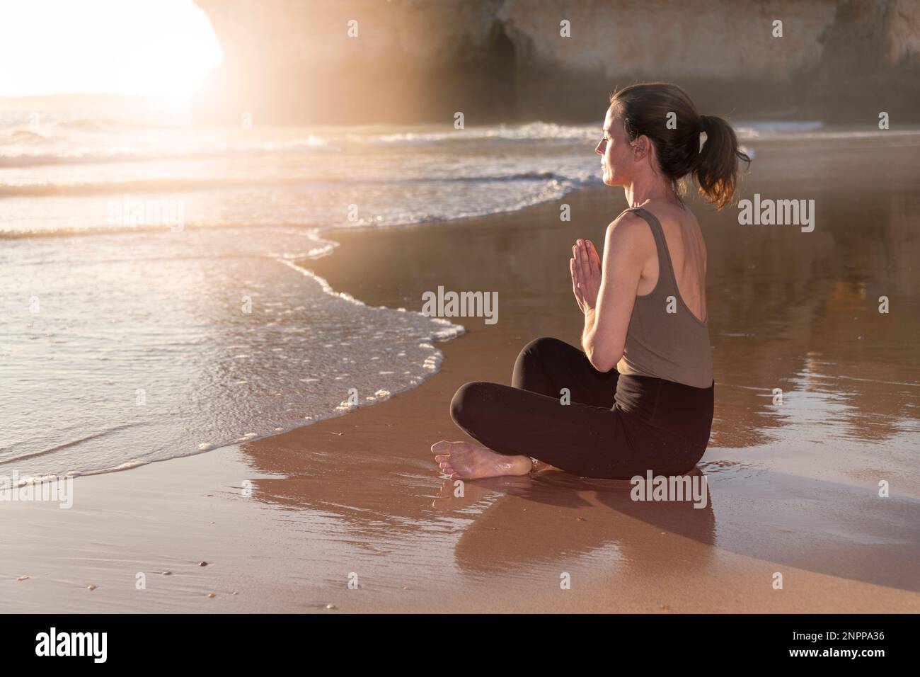 woman sitting in the lotus position on a beach, meditating and practicing yoga. Stock Photo
