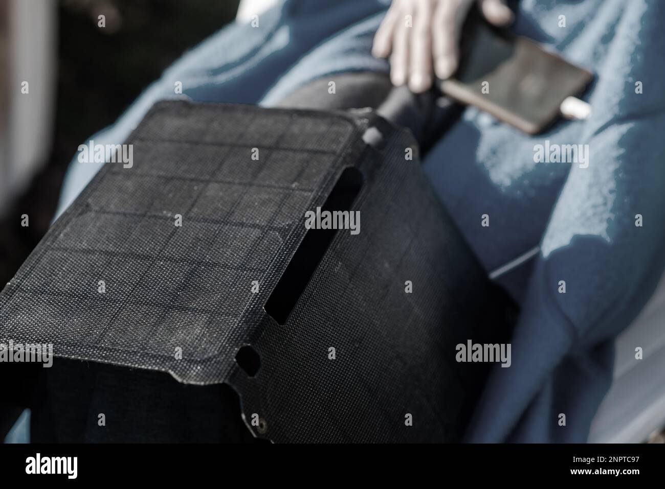 A portable solar battery rests on the legs of an unrecognizable woman. Ecological alternative energy concept. Stock Photo