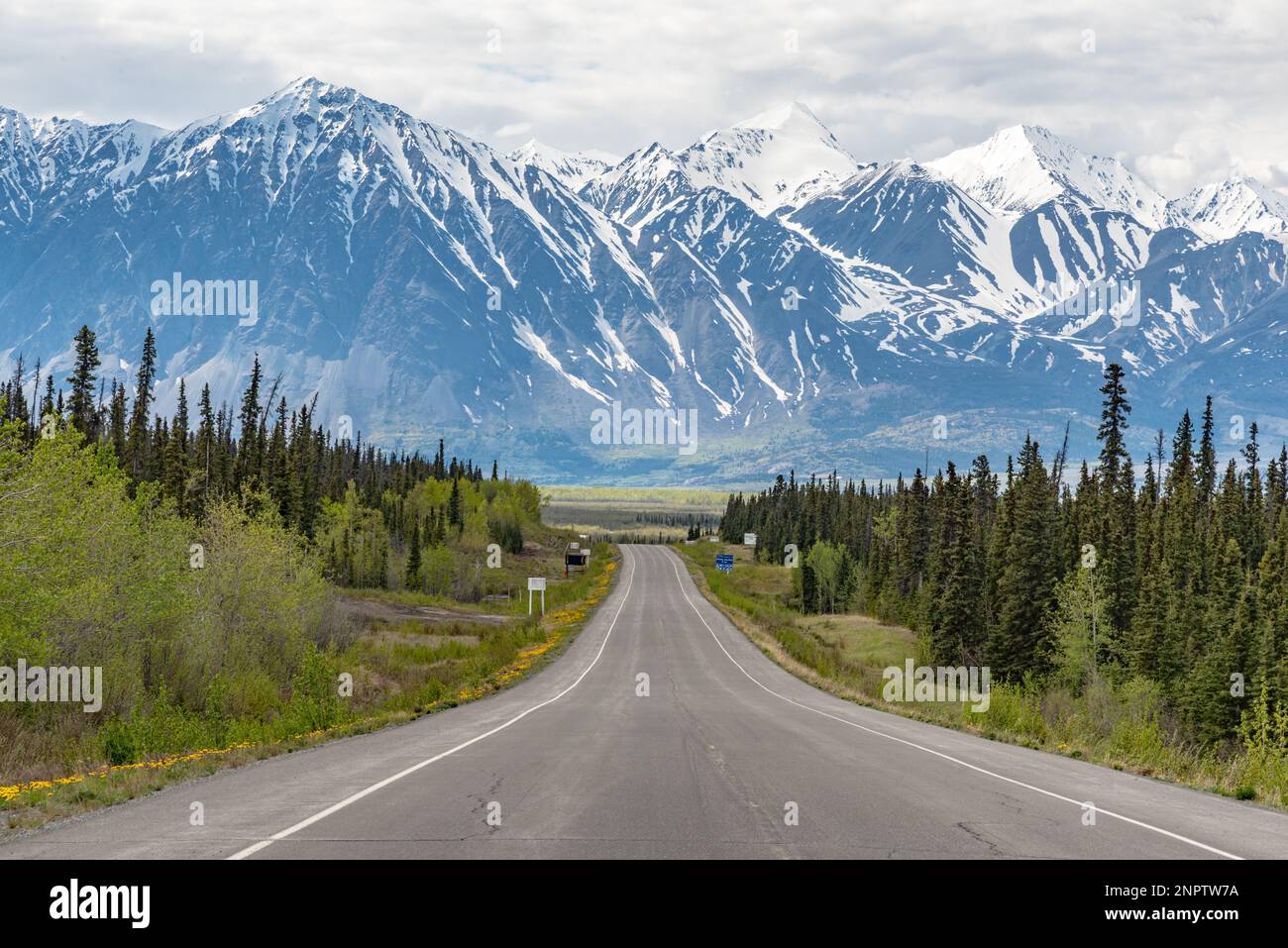 Alaska Highway driving into Haines Junction town in spring time with epic, huge mountains in far