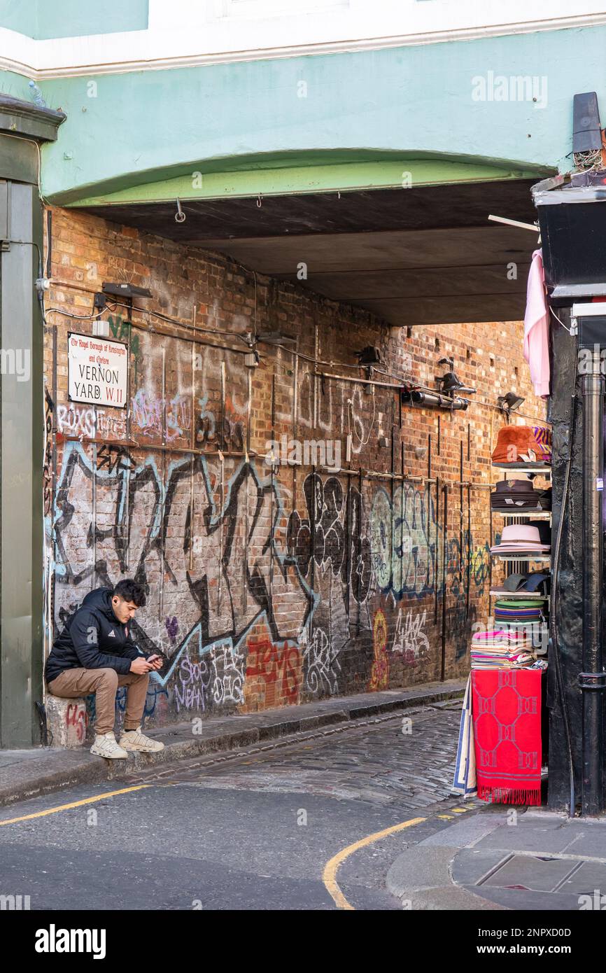 Man sitting by Vernon Yard gateway off the Portobello Road in Notting Hill district of London, England Stock Photo