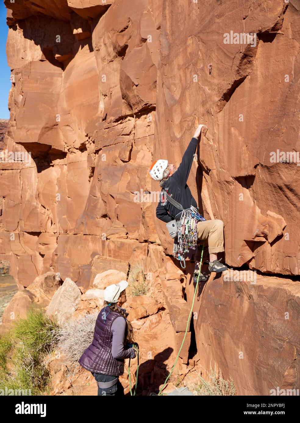 Adult male ascends a steep rock face. Moab, Utah Stock Photo
