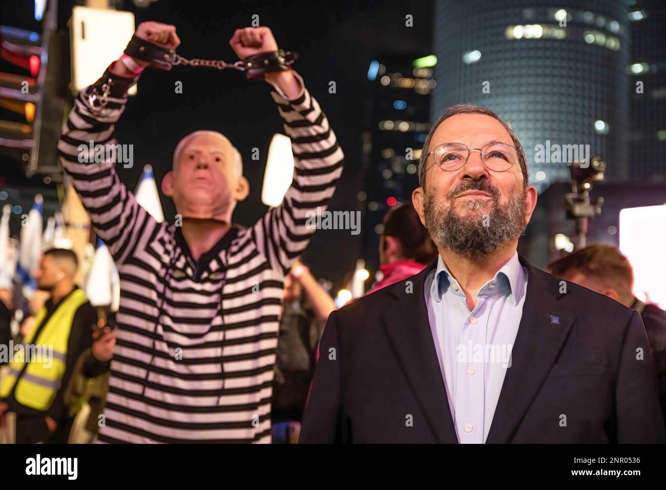 Tel Aviv, Israel. 25th Feb, 2023. Ehud Barak, former Prime Minister of Israel, looks on as he listen to a speech while a protestor dressed in a convict uniform and wearing a Benjamin Netanyahu mask lifts his handcuffed arms in the air during the demonstration. Over 150,000 people protested in Tel Aviv against Netanyahu's far-right government and its controversial legal reform. 21 demonstrators were arrested while blocking the Ayalon highway. Credit: SOPA Images Limited/Alamy Live News Stock Photo