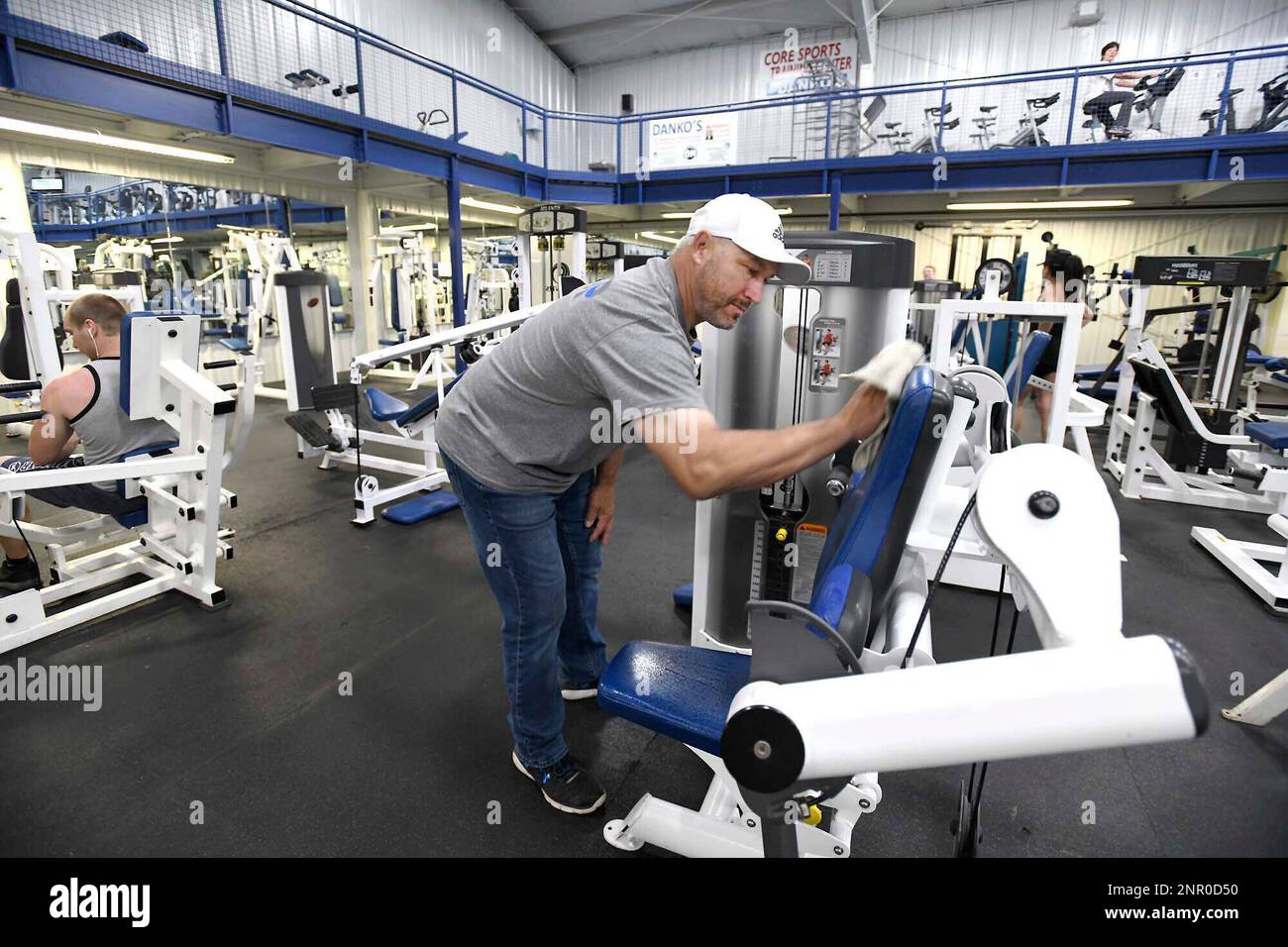 In this Monday, May 25, 2020 photo, Larry Danko wipes down a workout seat  at his business, Danko's All American Fitness in Plains Township, Pa.  Police and state regulators are cracking down