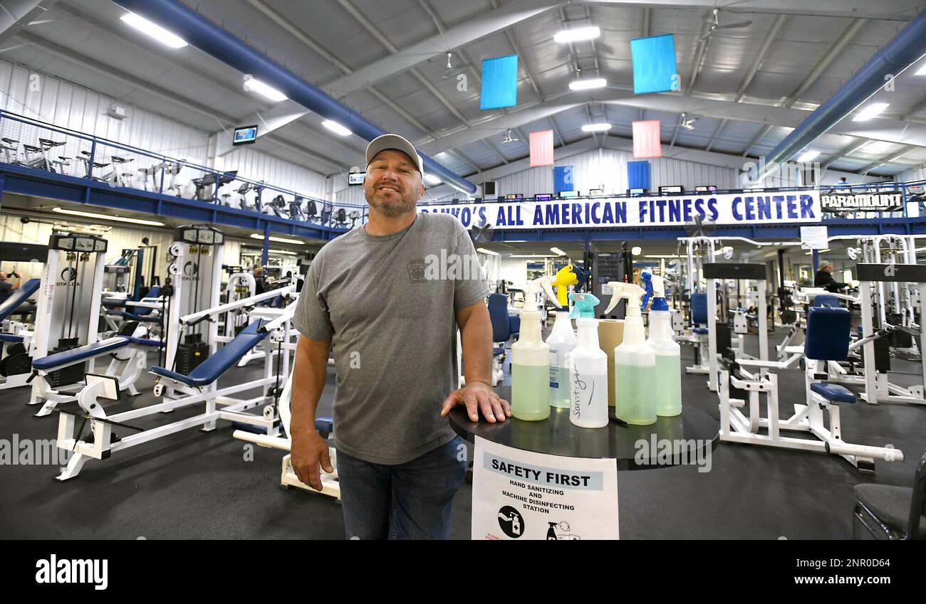 In this Monday, May 25, 2020 photo, Larry Danko wipes down a workout seat  at his business, Danko's All American Fitness in Plains Township, Pa.  Police and state regulators are cracking down