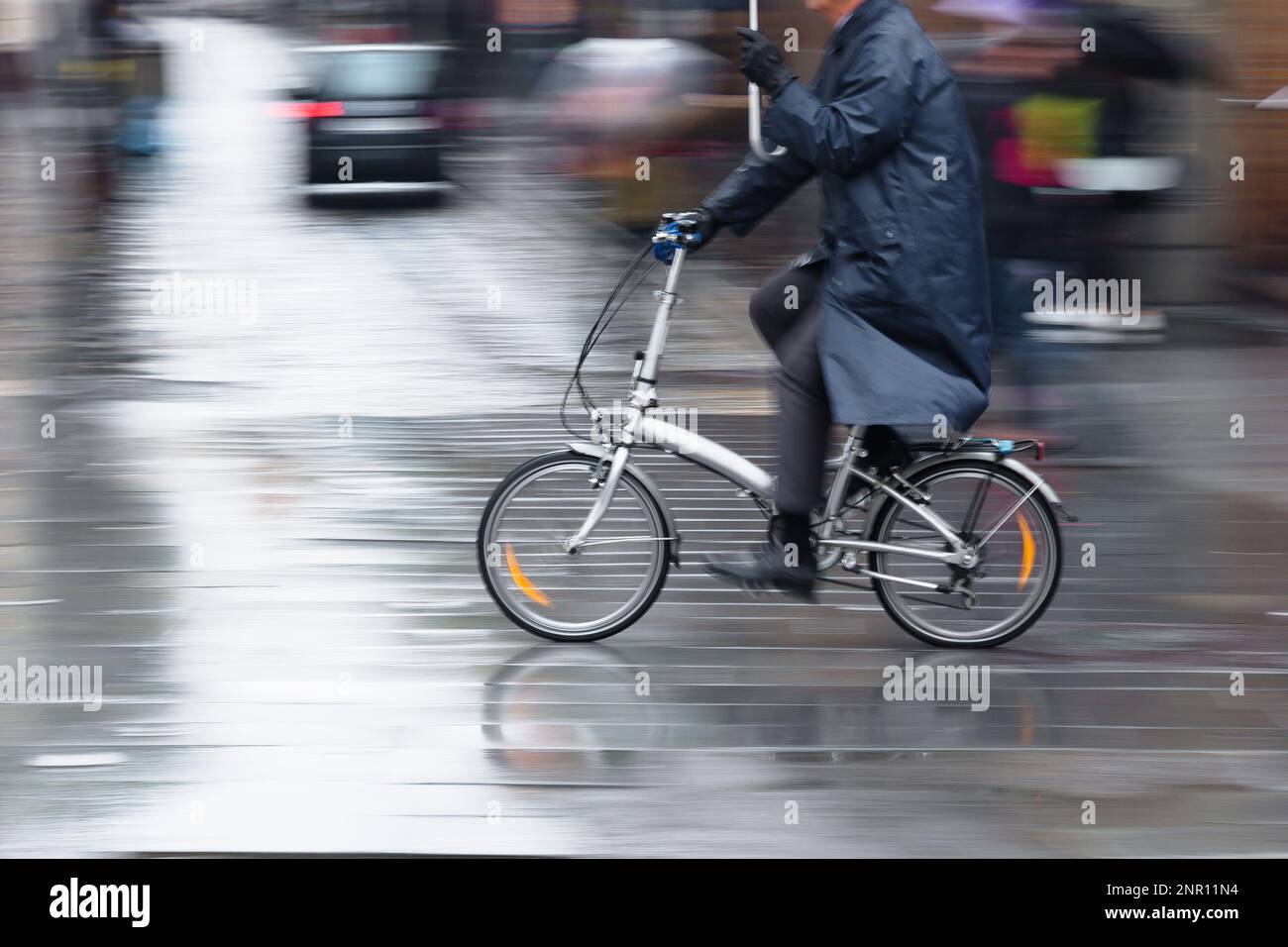 motion blur image of a man with umbrella riding a folding bicycle in the rainy city Stock Photo
