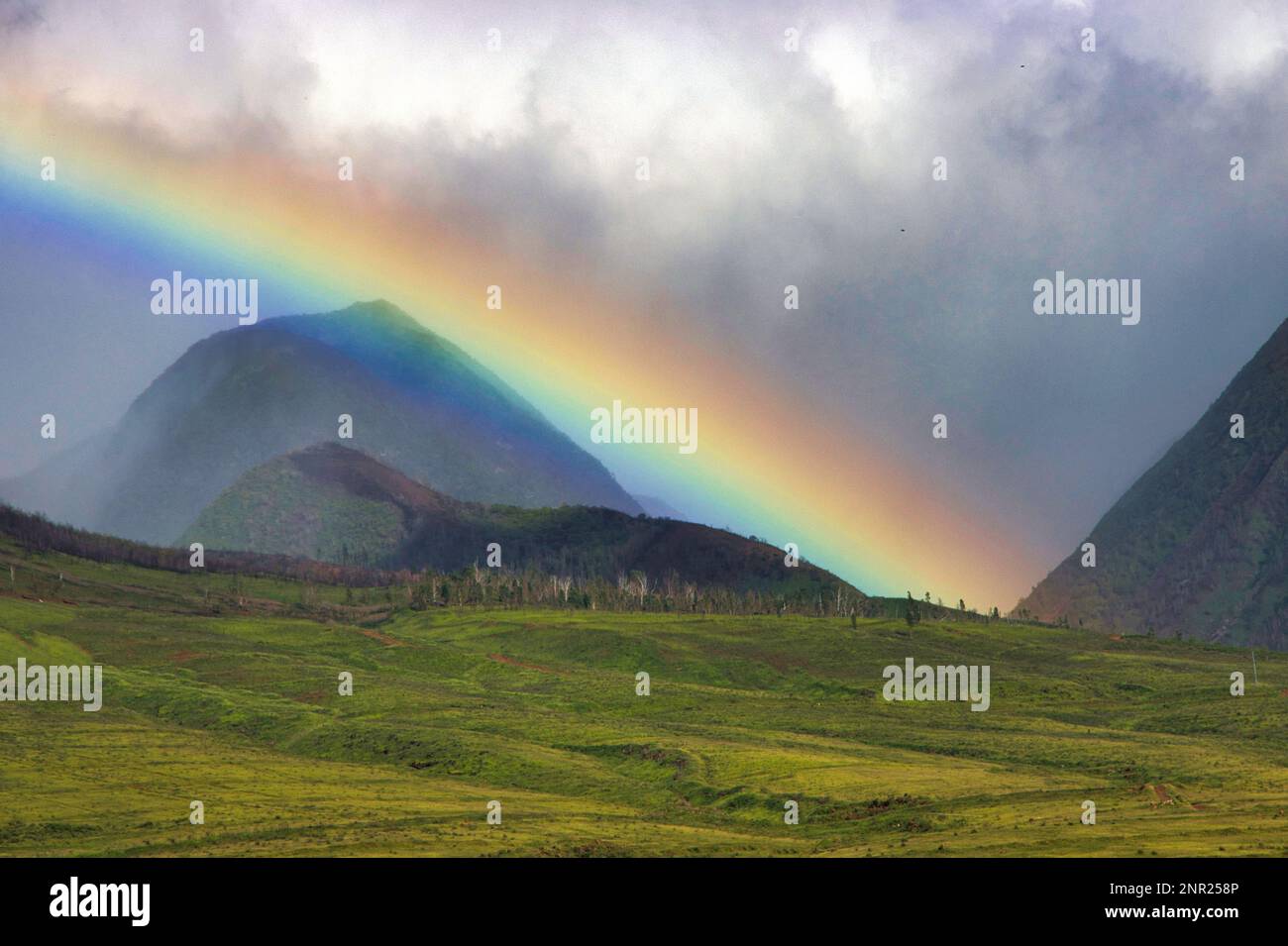 Low hanging glowing rainbow across the west maui mountains. Stock Photo