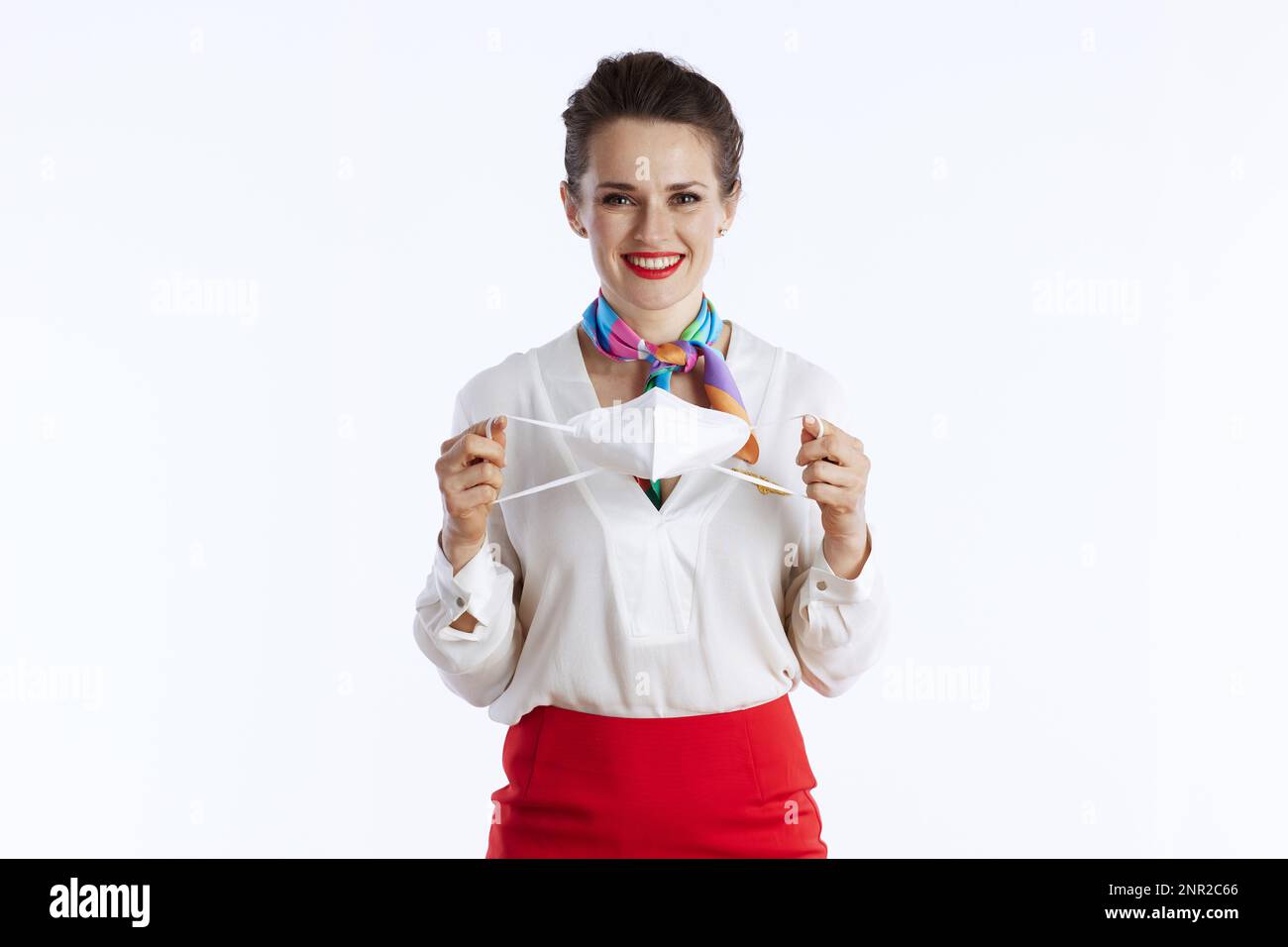 smiling modern flight attendant woman against white background in uniform with ffp2 mask. Stock Photo