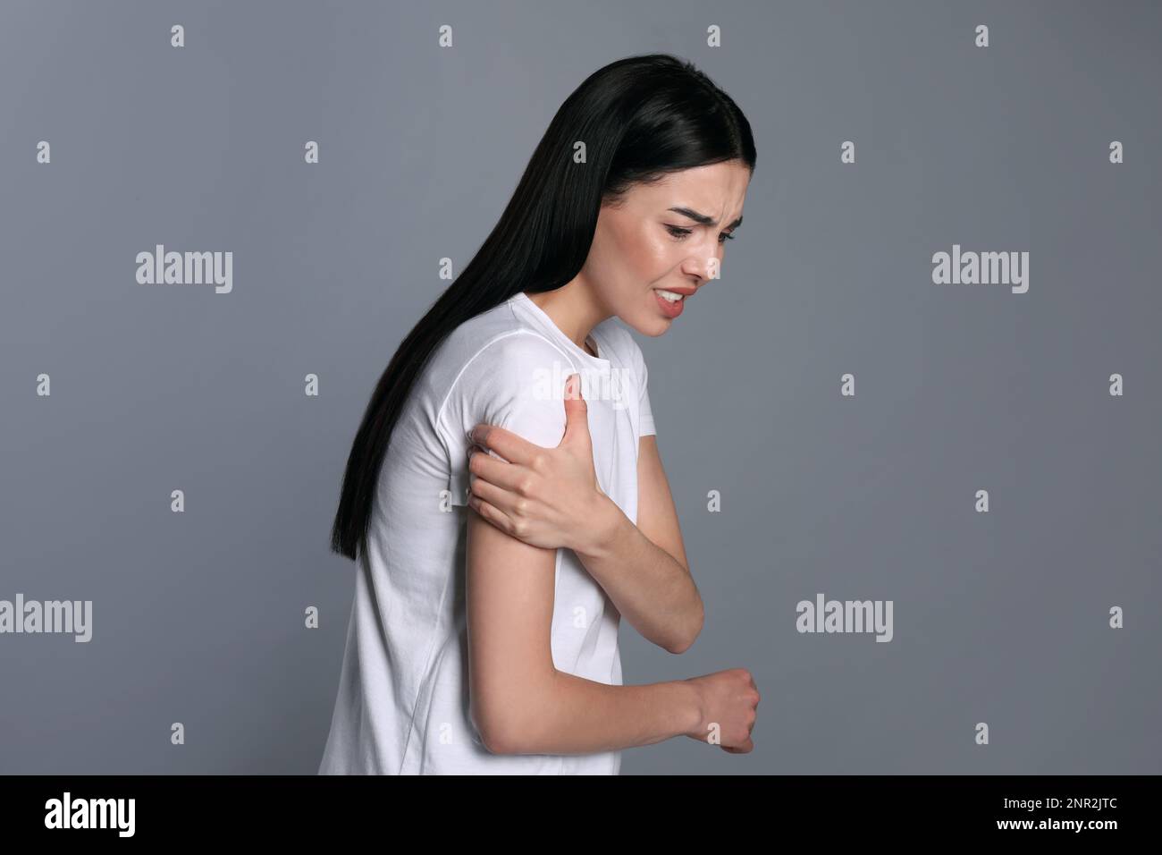 Woman suffering from shoulder pain on grey background Stock Photo