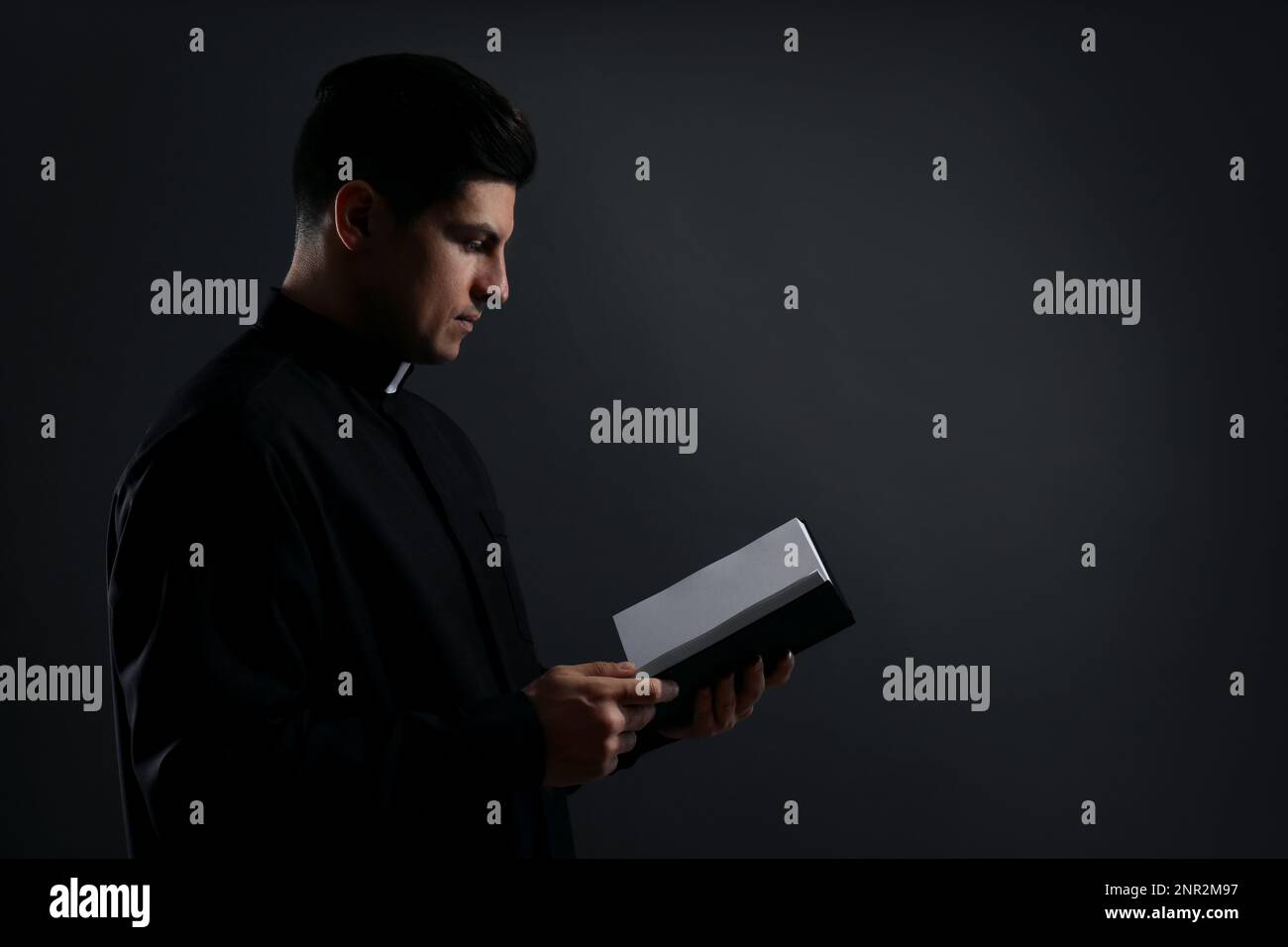 Priest with Bible on black background. Space for text Stock Photo
