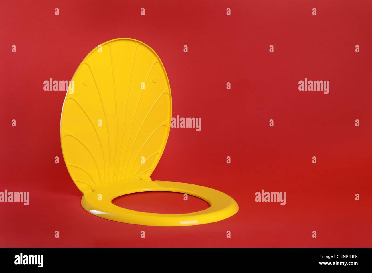 New yellow plastic toilet seat on red background, space for text Stock