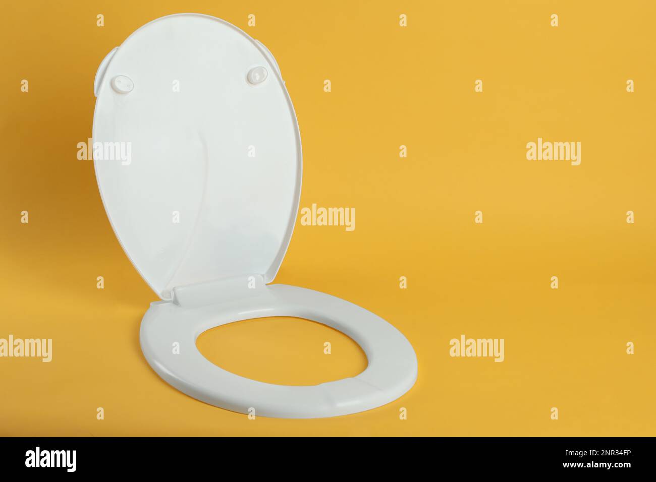 New white plastic toilet seat on yellow background, space for text Stock Photo