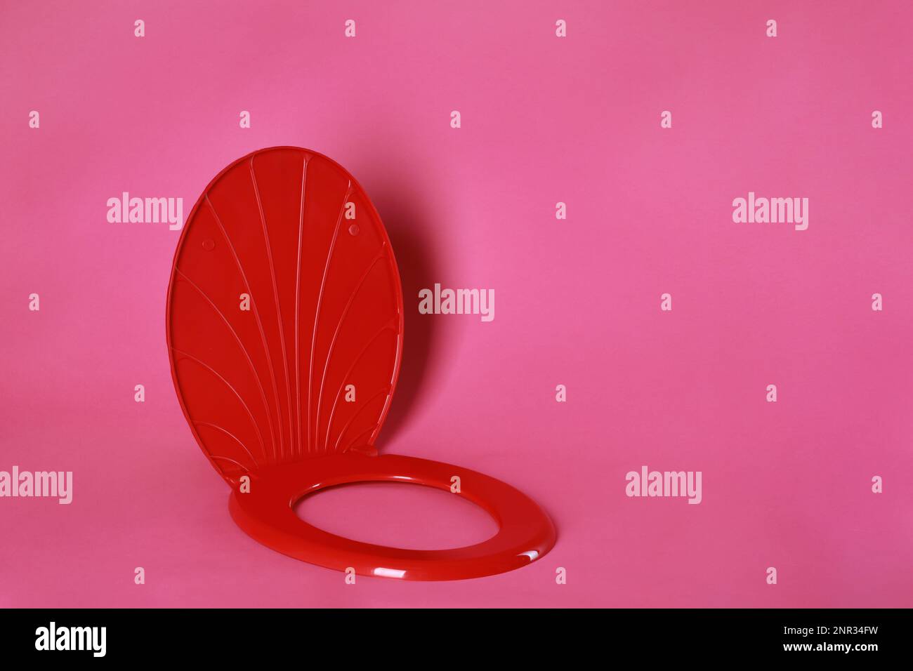 New red plastic toilet seat on pink background, space for text Stock Photo