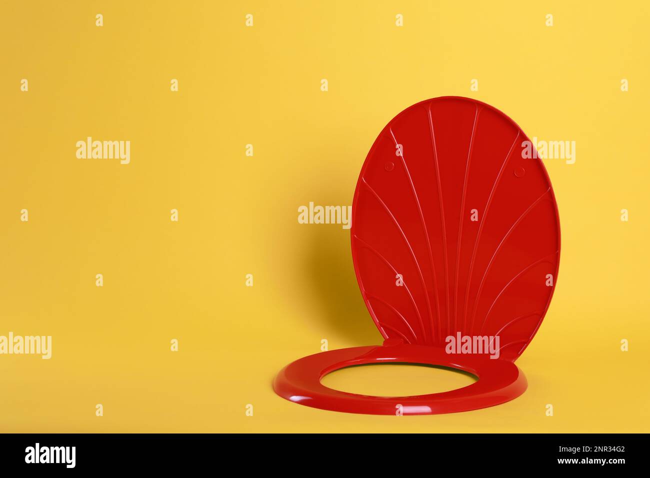 New red plastic toilet seat on yellow background, space for text Stock