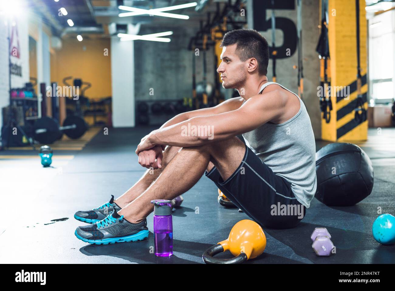 side view young man sitting floor near exercise equipments water bottle Stock Photo