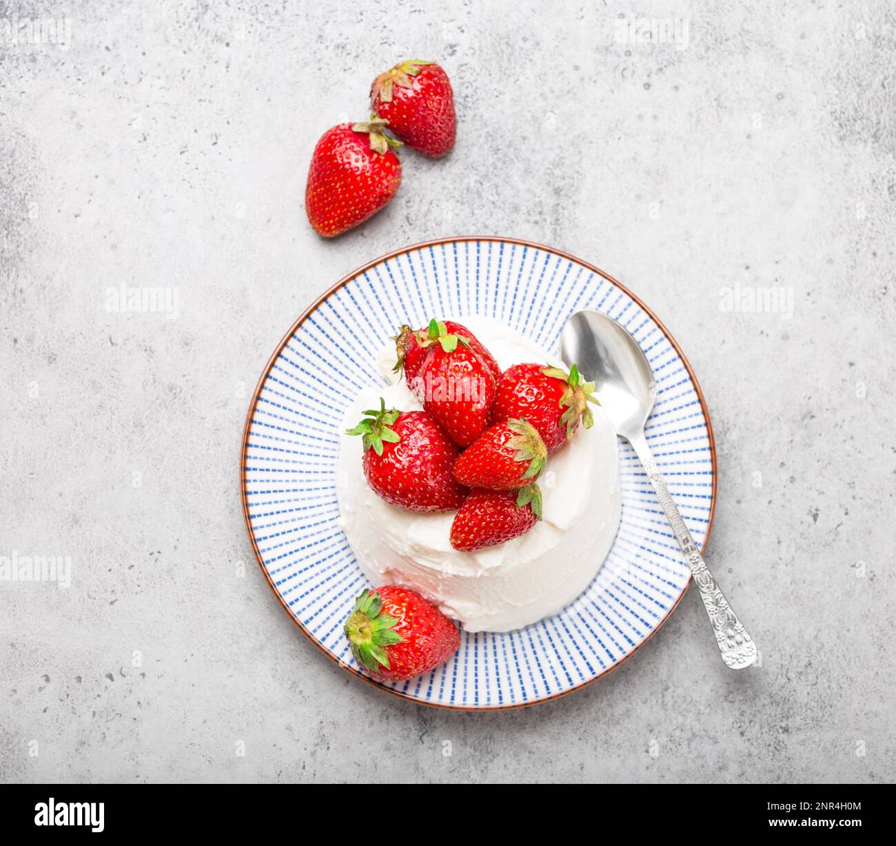 Top-view of fresh Italian cheese ricotta with strawberries on a plate with a spoon, grey rustic stone background, light summer dessert or snack, good Stock Photo