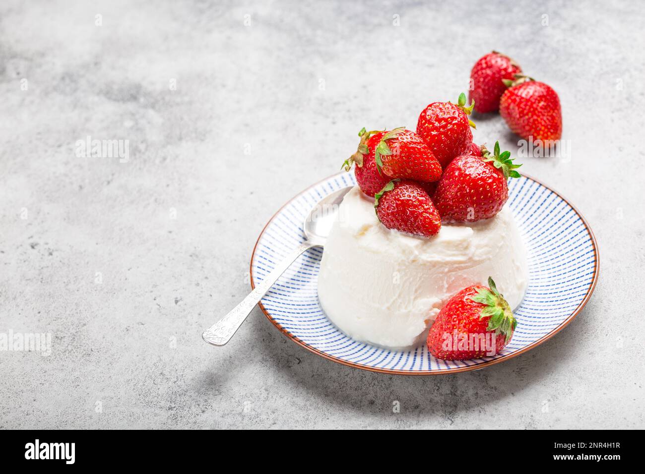 Close-up of fresh Italian cheese ricotta with strawberries on a plate with a spoon, grey rustic stone background, light summer dessert or snack, good Stock Photo