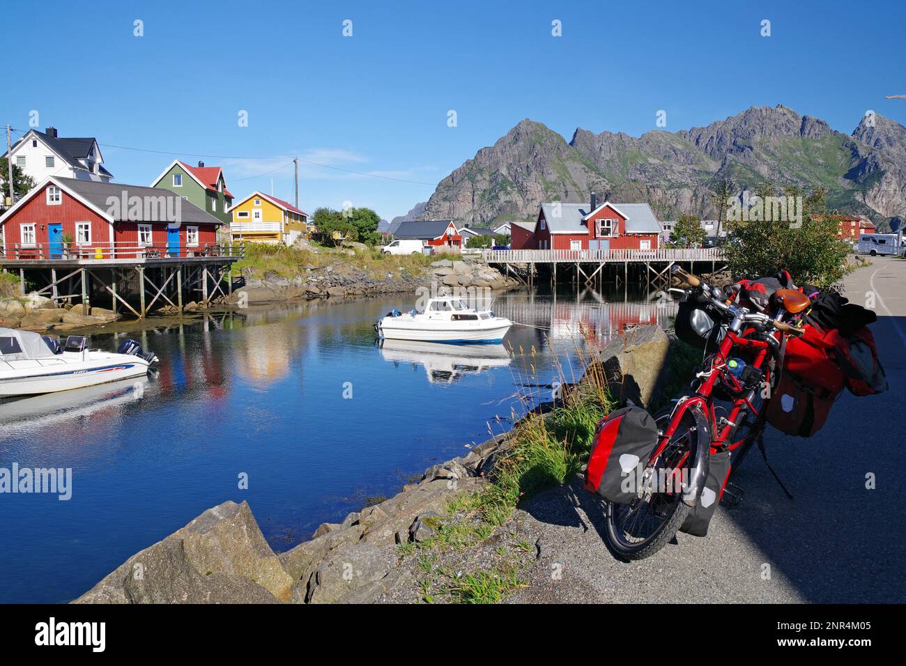 Different coloured hozhouses reflected in crystal clear sea water, packed touring bike, bicycle tourism, small leisure boats and rorbuer, Henningsvaer Stock Photo