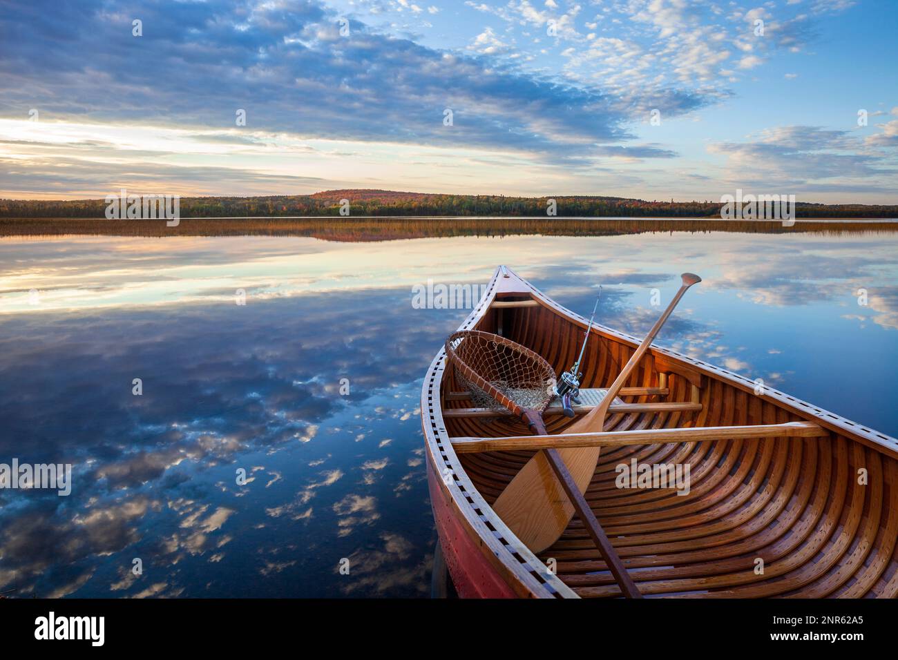 Wood canoe with vintage fishing rod and net on calm lake with hills with trees in autumn color in northern Minnesota Stock Photo