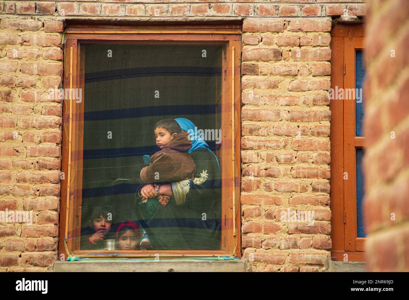 Srinagar, India. 25th Feb, 2023. Kashmiri Muslim woman with her children watch the funeral ceremony of Sanjay Sharma a Kashmiri Hindu bank security guard who was shot dead by suspected militants in Pulwama South of Indian administered Kashmir. Police said suspected militants opened fire on Sanjay Sharma while he was on his way to a local market in Achan village Pulwama district. Credit: SOPA Images Limited/Alamy Live News Stock Photo