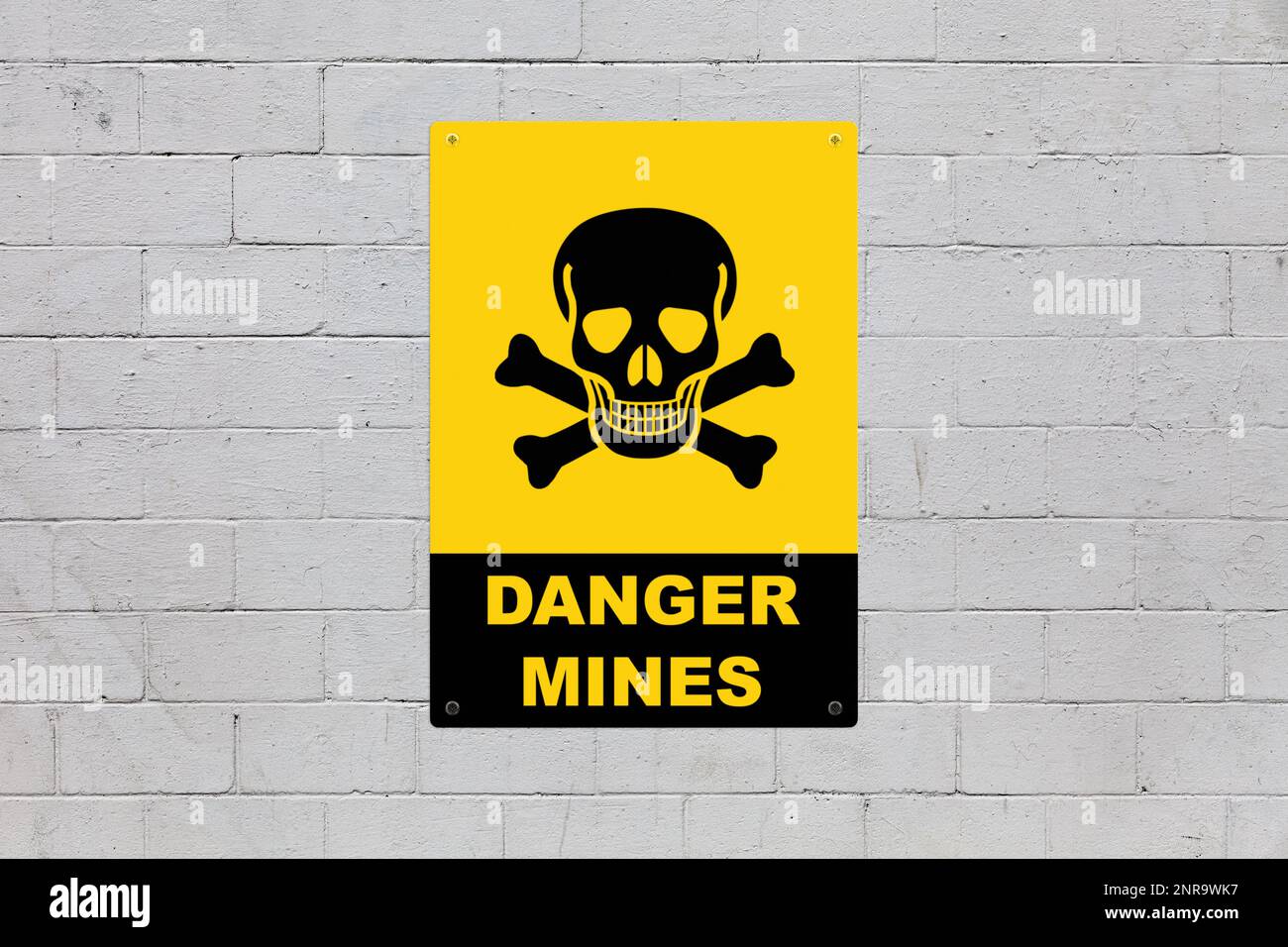 Yellow warning sign screwed to a brick wall to warn about a threat. In the middle of the panel, there is a skull and bones symbol and the message sayi Stock Photo