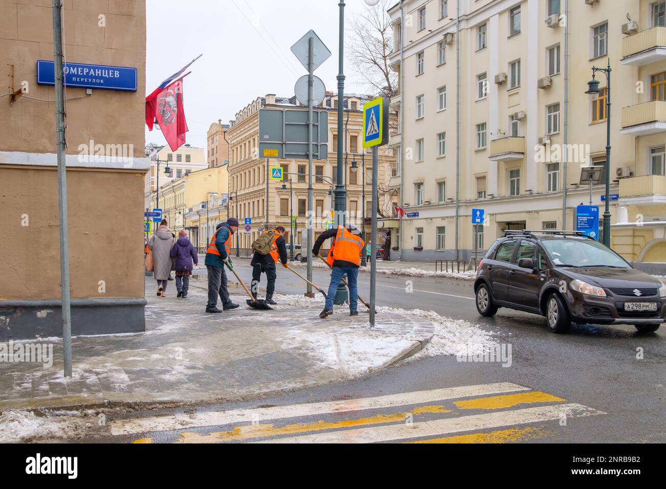 Moscow. Russia. February 25, 2023. Workers in orange vests shovel snow off the sidewalk on a city street on a cloudy winter day. Stock Photo