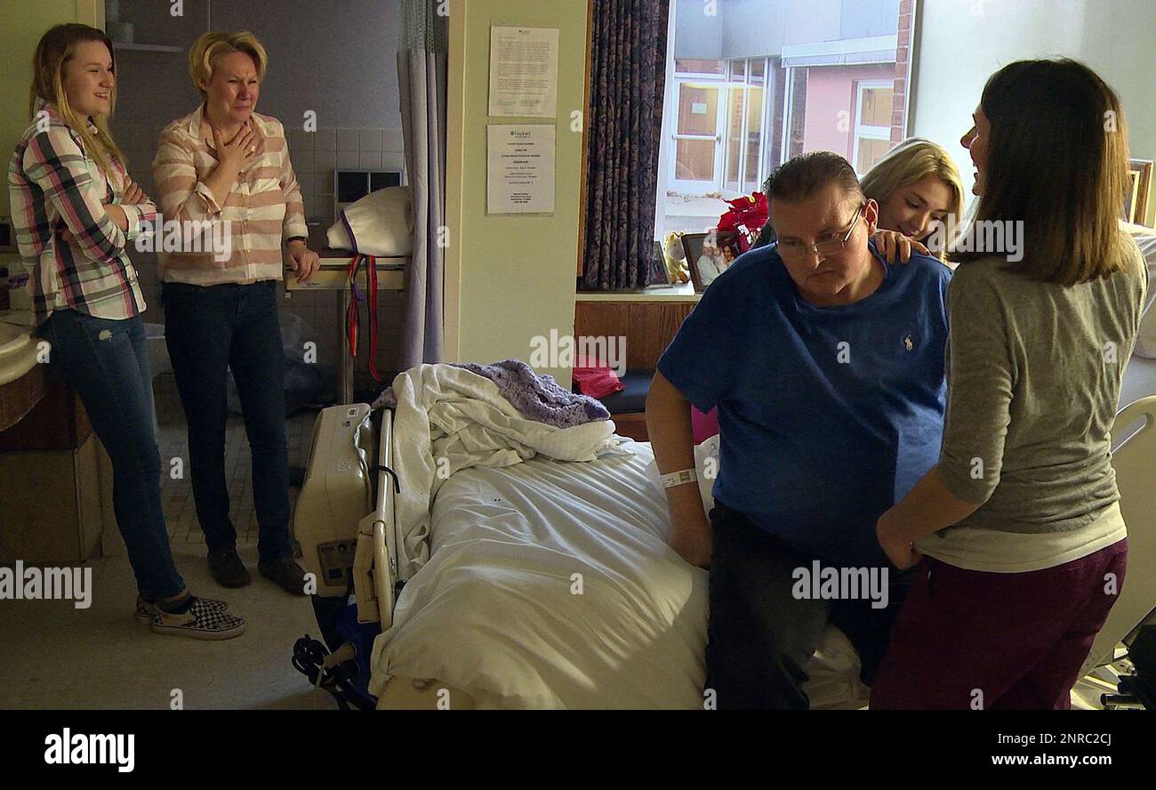 In this Jan. 10, 2020, photo Amelia and Malgorzata Pawulski, from left,  react as their father and husband Richard Pawulski sits up with help from  physical therapist Caitlin Boland and occupational therapist