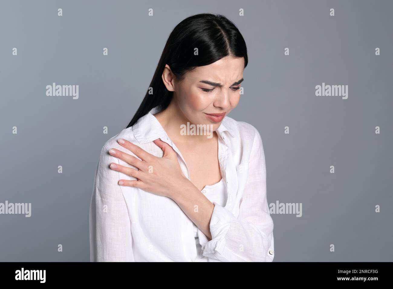 Woman suffering from shoulder pain on grey background Stock Photo