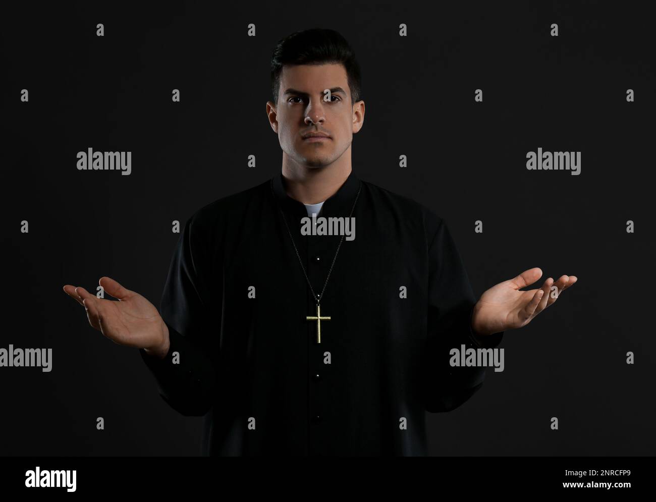 Priest wearing cassock with clerical collar on black background Stock Photo