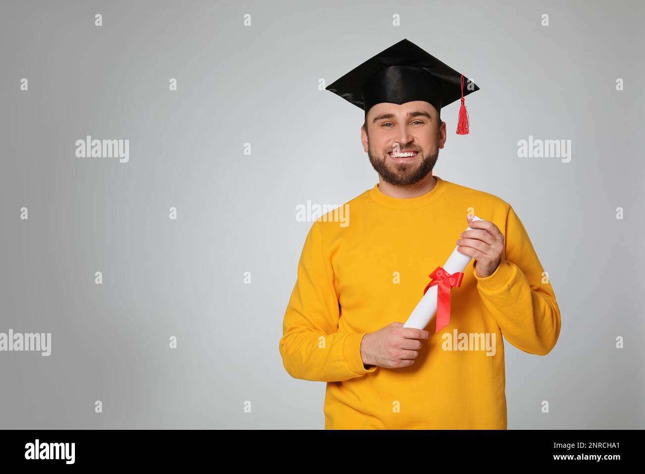 Happy student with graduation hat and diploma on grey background. Space ...