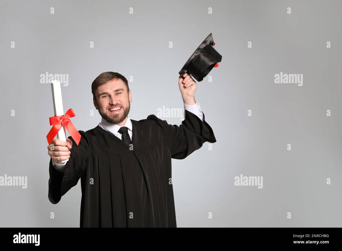 Happy student with graduation hat and diploma on grey background. Space ...