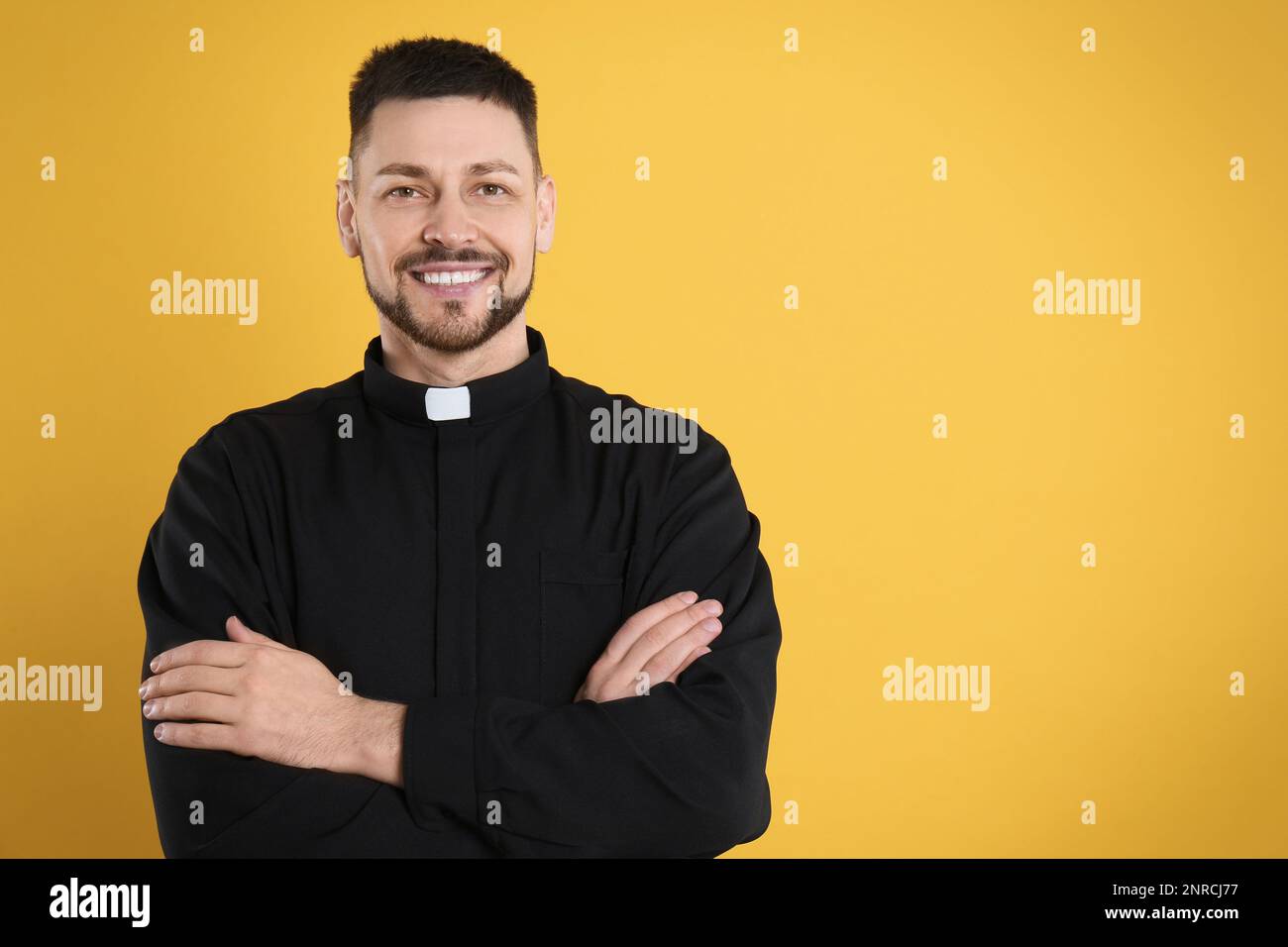 Priest wearing cassock with clerical collar on yellow background, space for text Stock Photo