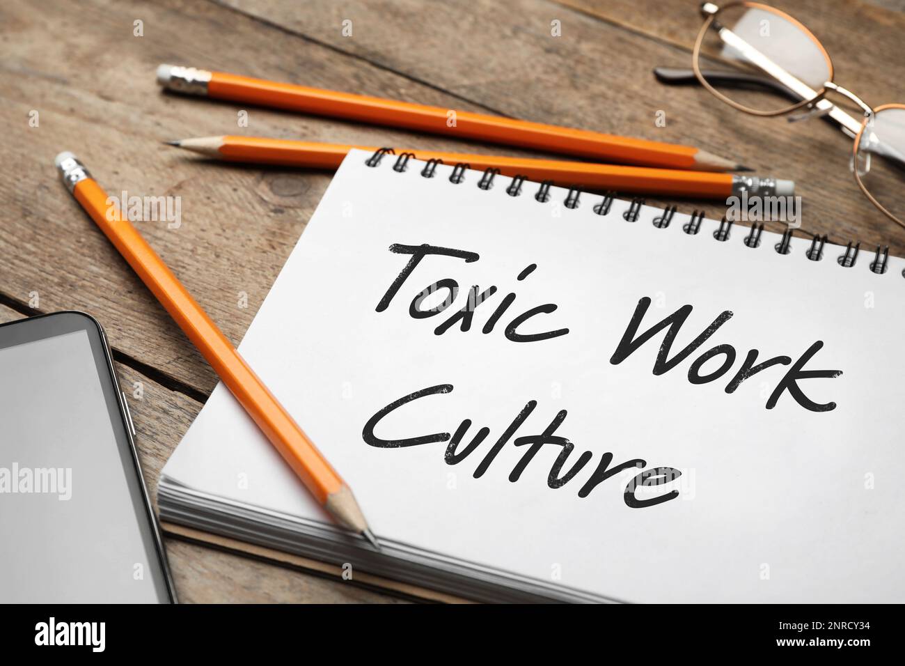 Notebook with text Toxic Work Culture on wooden table, closeup Stock Photo