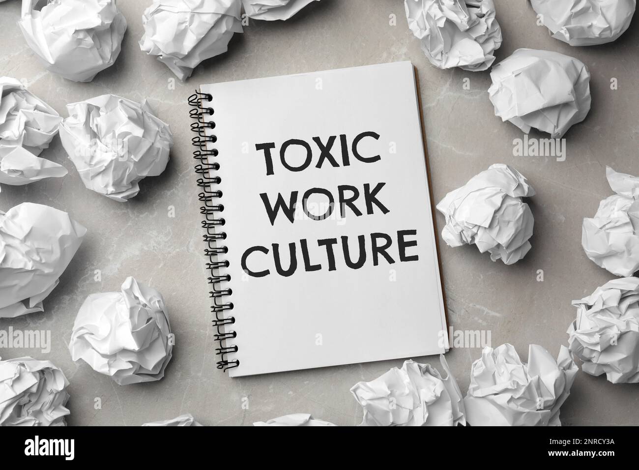 Notebook with text Toxic Work Culture and crumpled paper on grey marble table, flat lay Stock Photo