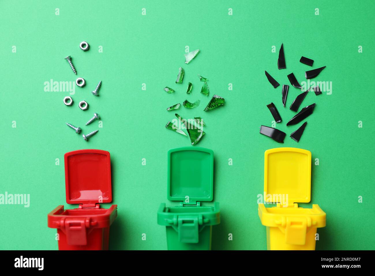 Mini recycling bins and different garbage on green background, flat lay