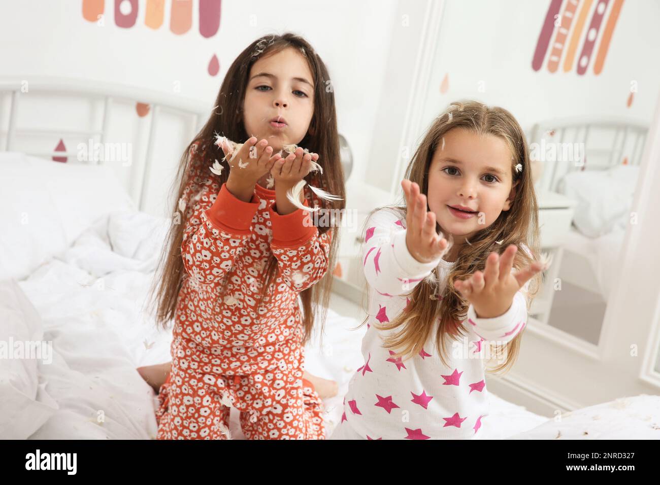 Cute little girls in pajamas playing with feathers on bed at home ...