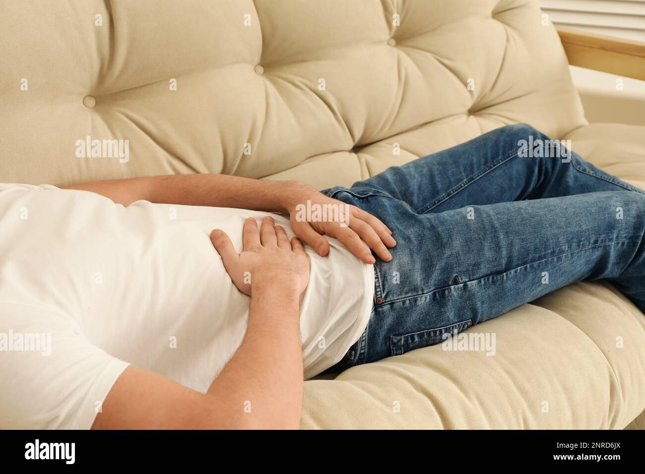 Man suffering from pain in lower right abdomen on sofa at home, closeup