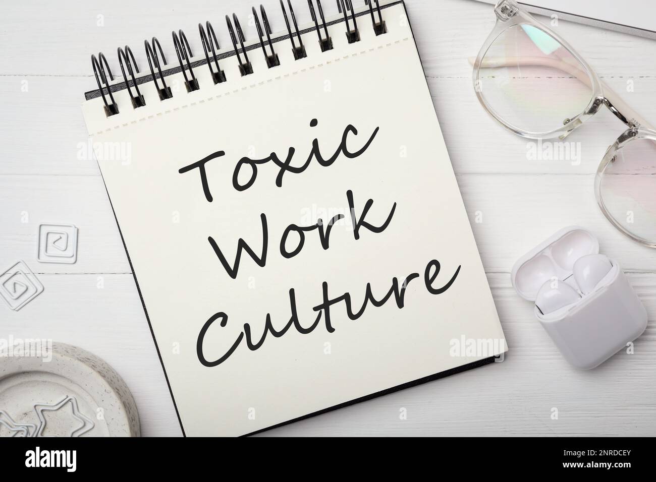 Notebook with text Toxic Work Culture on white wooden table, flat lay Stock Photo