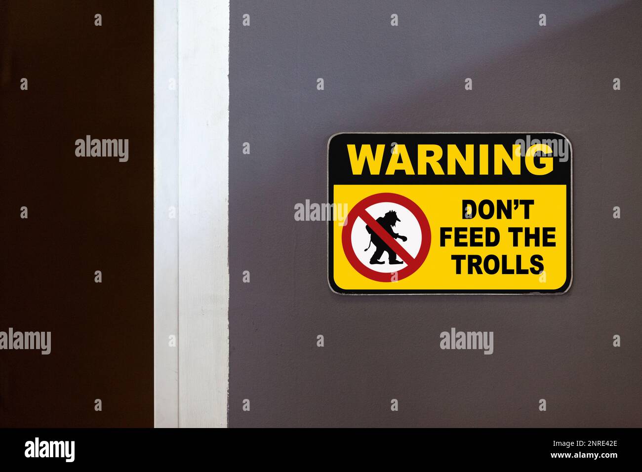 Yellow and black warning sign on the side of an open door stating in 'Warning - Don't feed the Trolls'. Stock Photo